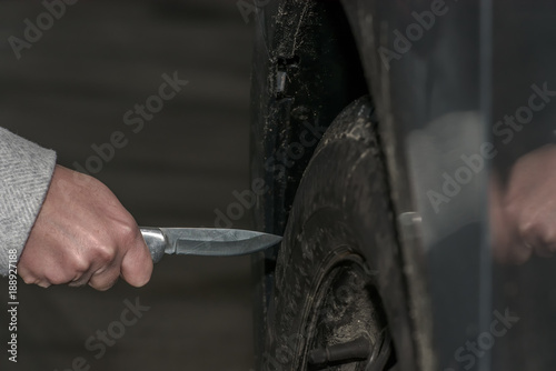 A woman holds a knife in her hand and wants to sting with it in a car tire. Slashing into a car tire. Concept: vandalism and crime