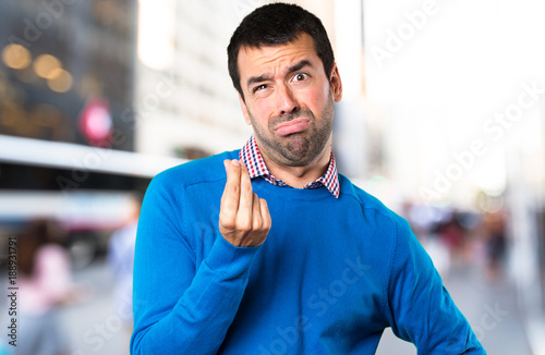 Handsome young man making money gesture on unfocused background