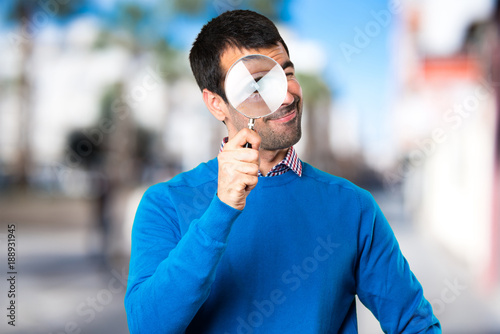 Handsome young man with magnifying glass on unfocused background
