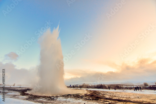 Strokkur geysir wowing the small group of tourists who surround it as it explodes out of the ground at dawn.