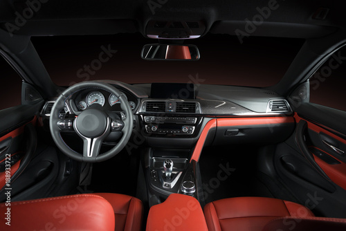 Modern luxury car Interior - steering wheel, shift lever and dashboard. Car interior luxury.Steering wheel, dashboard, speedometer, display. Red and black perforated leather cockpit © gargantiopa