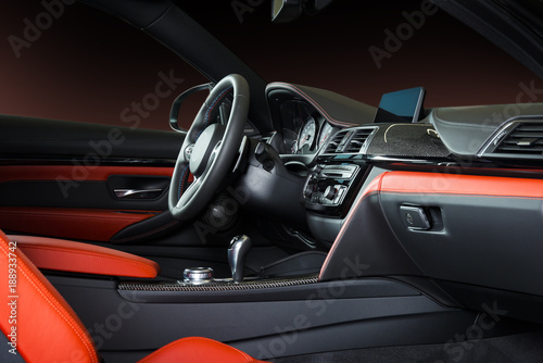 Modern luxury car Interior - steering wheel, shift lever and dashboard. Car interior luxury inside. Steering wheel, dashboard, speedometer, display. Red and black leather cockpit © gargantiopa