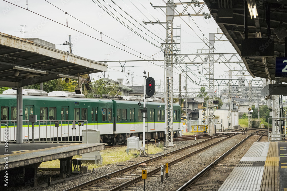 Green train enters local station in Kyoto, Japan. Transport backround featuring details of railroad and station infrastructure.