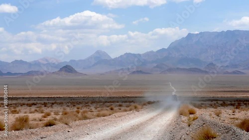 car is moving along a deserted road, raising a lot of dust, chasing a ridge on the horizon, beautiful white clouds