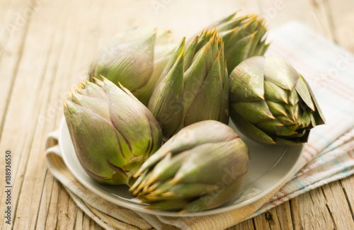 Five artichokes on the white plate on the wooden table