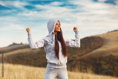 Young sport woman with raised arms motivates herself in nature