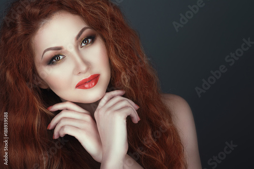 Close up portrait of a gorgeous smiling red headed woman with beautiful make up, her hands crossed under her chin. Isolated on grey background. Copy-space