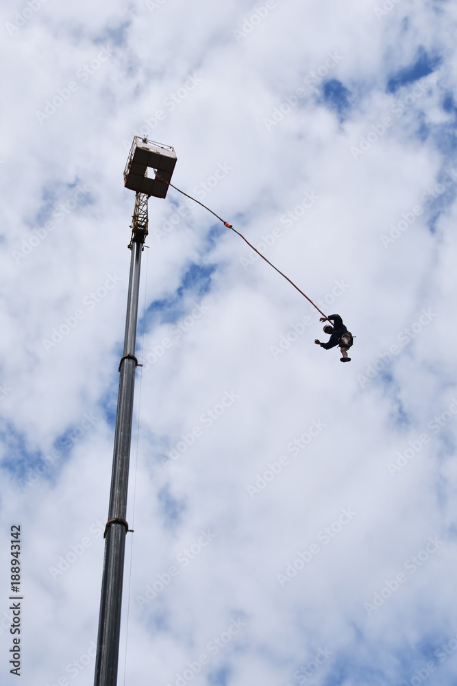 Bungee juming - seen from the ground silhouette of a young man rushing down from a high crane platform Bungee juming - seen from the ground silhouette of a young man rushing down from a high crane platform