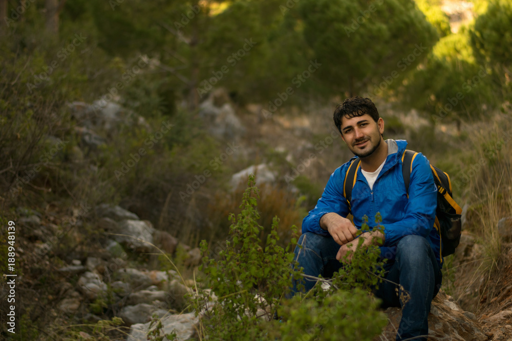 Traveler man in the forest with a backpack sits on a stone looking at the camera Traveler man in the forest with a backpack sits on a stone looking at the camera