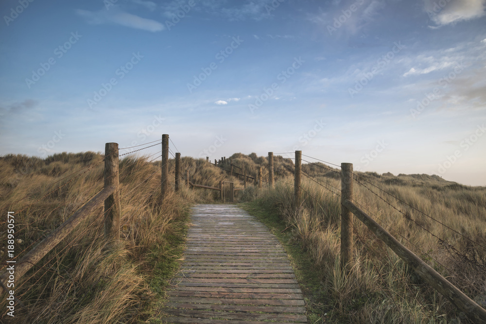 Beautiful sunrise landscape image of sand dunes system over beach with wooden boardwalk