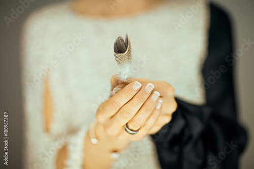woman hands holding single feather in her hands, light pastel colors can be used as romantic background