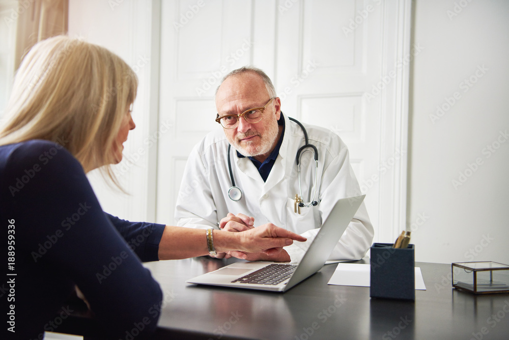 Woman asking doctor pointing at laptop in office Woman asking doctor pointing at laptop in office