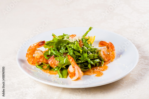 Salad with arugula, shrimps, salmon and parmesan cheese on white plate