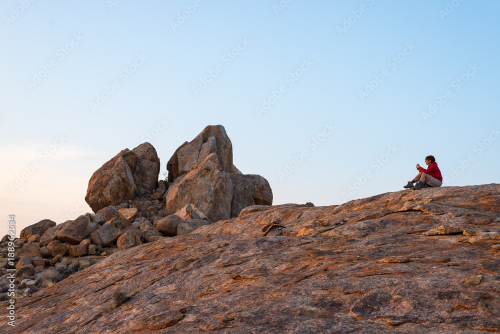 Woman sitting on rocks and looking at expansive view over the scenic Namib desert at dusk time. Travel in the Namib Naukluft National Park, Namibia, Africa.