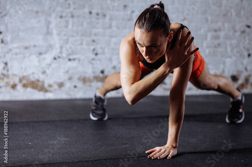 young beautiful woman in sportswear doing one handed plank while trainnig at cross fit gym photo