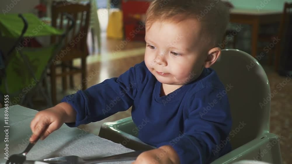 the kid is having lunch at the restaurant. In the hands of a spoon and fork the kid is having lunch at the restaurant. In the hands of a spoon and fork