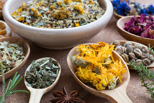 Dried calendula on a wooden spoon, with other herbs in the background