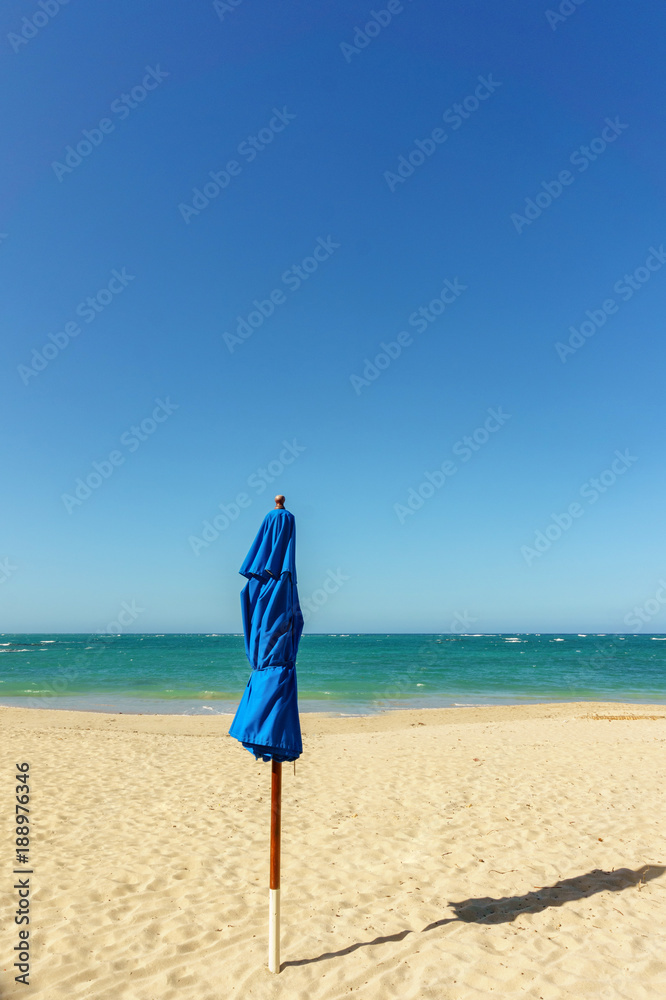 closed blue beach umbrella with shadow on the sandy beach closed blue beach umbrella with shadow on the sandy beach