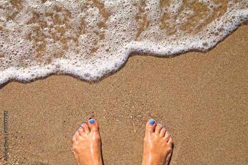 Vacation concept, women foot near sea foam at gold sand