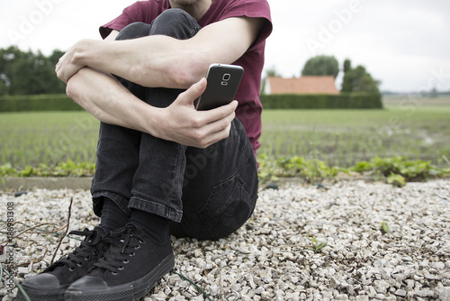 An anonymous young man or boy holding his phone and looking at it. A concept about struggling with yourself, being mentally and physically tangled up, autism, online bullying and suicide thoughts.