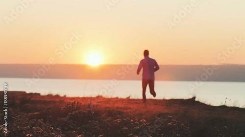 young man trail runner training outdoors in the fields, sunset in lake background 