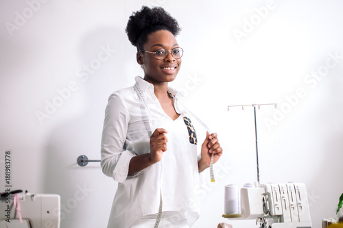 smiling african seamstress looking at camera with sewing machine photo