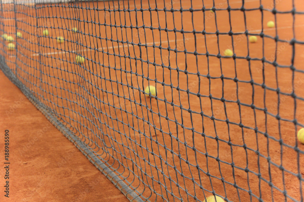 Tennis balls on red court with gray net Tennis balls on red court with gray net
