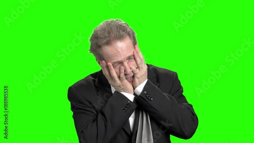 Extremely stressed furious businessman. Frustrated irate businessman in suit screaming and touching head with both hands, green hroma background. photo