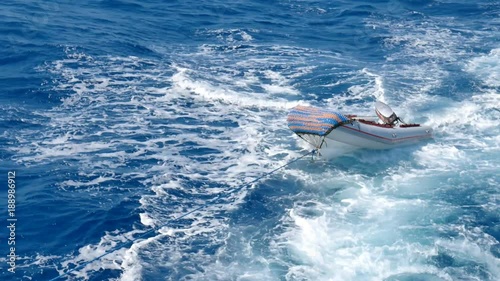 Ship tows a small boat behind it connected by a thick rope. Motor boat swings on the waves 4k. 