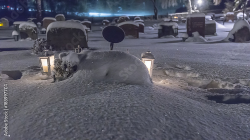 Gravlyktor som lyser upp snön vid en grav på en snöig kyrkogård i Stockholm photo