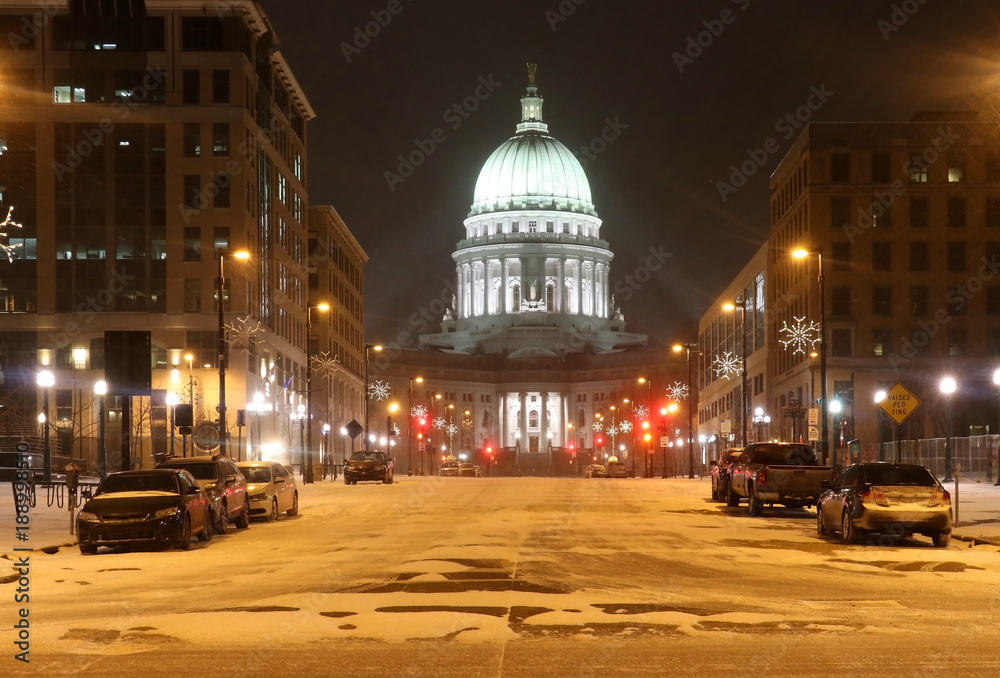 Beautiful snowy winter night. Madison, the capitol of Wisconsin downtown street view with parked cars and Wisconsin state capitol building glowing in the blizzard night. Wisconsin state, Midwest USA.