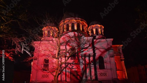 Smooth sliding shot of St. Michael the Archangel Church (Soboras) illuminated by various colors at night in Kaunas, Liberty Boulevard, Lithuania. photo