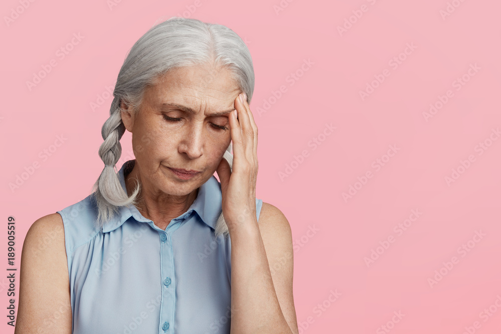 Frustrated female pensioner has headache as worries about something, has problems, looks unhappily down, poses against pink background with copy space for your promotional text. Old people, health Frustrated female pensioner has headache as worries about something, has problems, looks unhappily down, poses against pink background with copy space for your promotional text. Old people, health