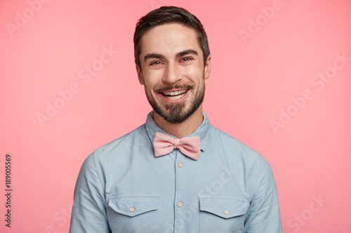 Portrait of handsome bearded young brunet male rejoices his promotion, going to celebrate this event with close friends, dressed elegantly, poses against pink background. Positive human emotions photo