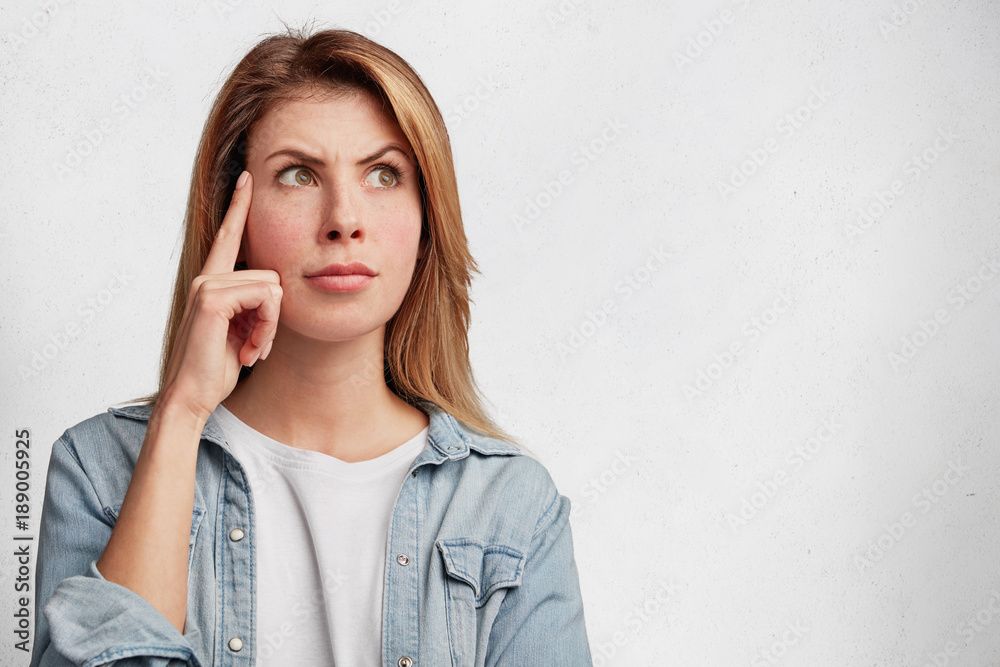 Isolated shot of attractive female generates new idea in mind, looks thoughtfully upwards, has attentive concentrated look, isolated over white background with copy space for your promotional text Isolated shot of attractive female generates new idea in mind, looks thoughtfully upwards, has attentive concentrated look, isolated over white background with copy space for your promotional text