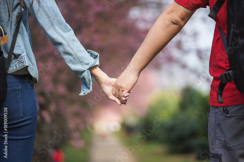 young couple in love holding hand together walking in a beautiful park with romantic nature background