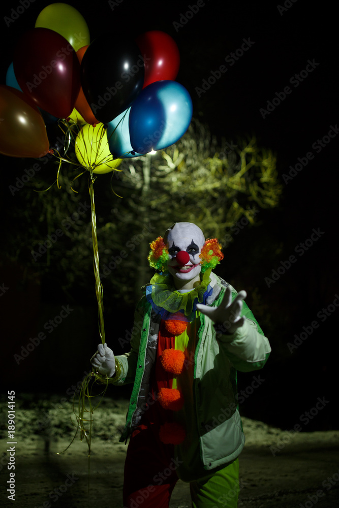 Photo of smiling clown with colorful balloons at night