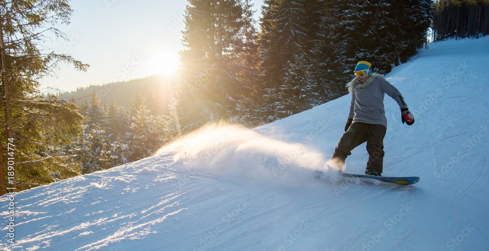 Φωτογραφία Full length shot of a female snowboarder skiing on snowy slope on the dawn in th