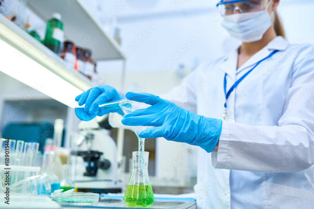 Portrait of female scientist wearing protective gloves pouring colored liquids to test tubes while studying chemicals in medical laboratory, focus on hands Portrait of female scientist wearing protective gloves pouring colored liquids to test tubes while studying chemicals in medical laboratory, focus on hands