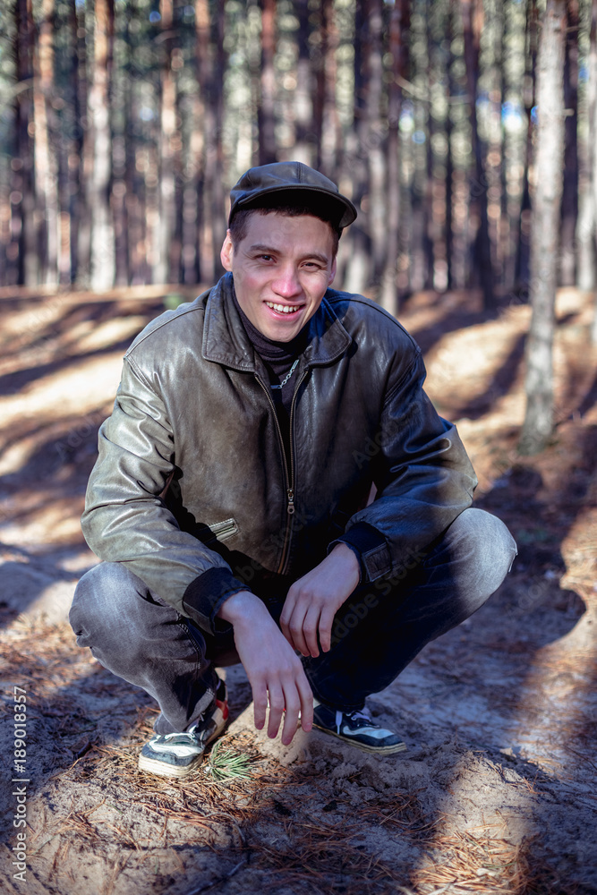 A guy in a leather jacket and cap sits on a road in a pine forest. A guy in a leather jacket and cap sits on a road in a pine forest.