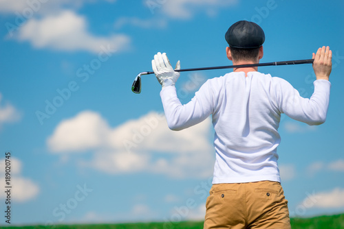 Golfer in a field with a golf club on his shoulders resting after a successful game