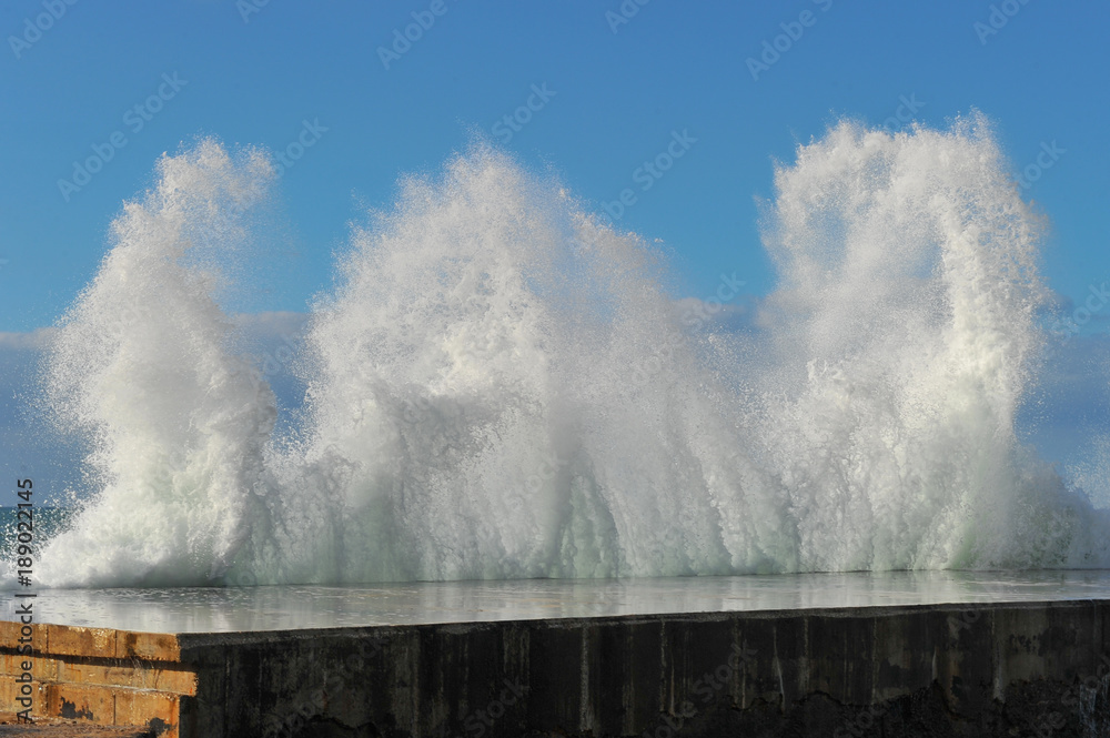 Waves breaking over coastal cliffs and breakwater during the storm, making a big splash of seawater