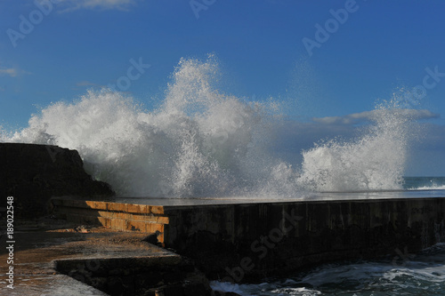 Waves breaking over coastal cliffs and breakwater during the storm, making a big splash of seawater
