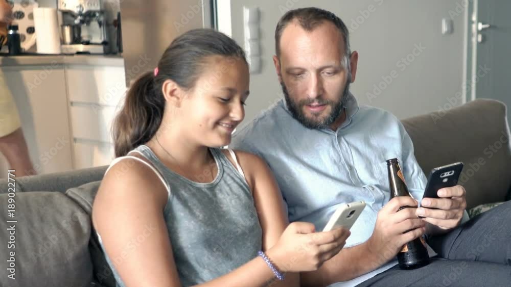 Father with his daughter talking and using smartphone on sofa at home
