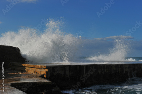 Waves breaking over coastal cliffs and breakwater during the storm, making a big splash of seawater