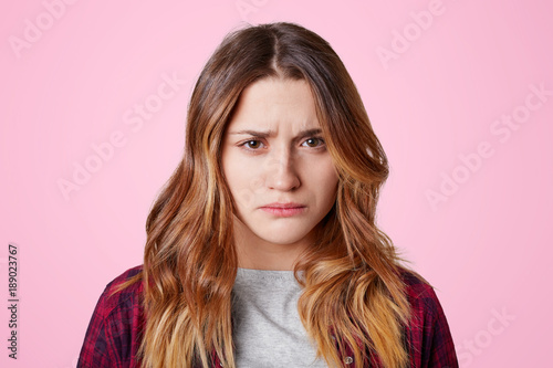 Attractive offended female with dissatisfied expression, curves lips, going to cry as being abused by close person, didn`t expect such bad attitude towards her, isolated over pink background photo