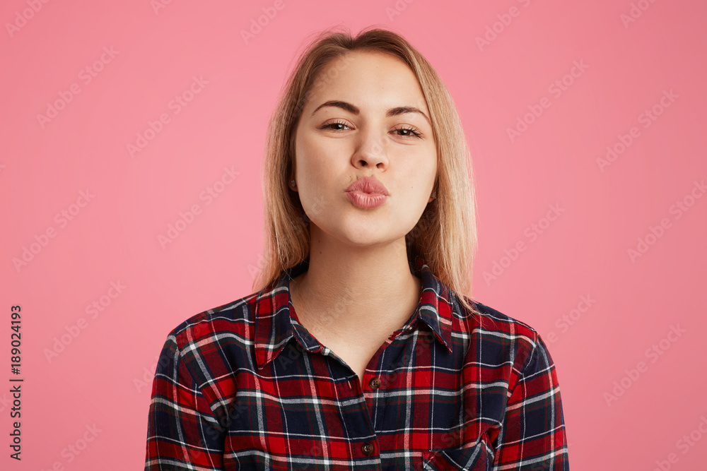 Horizontal shot of beautiful female with rounded lips, going to kiss boyfriend, expresses great love and good feelings, isolated over pink background. People, body language and facial expressions