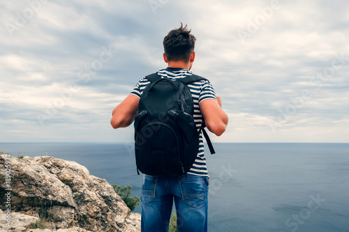 male traveler with a backpack on her back looking at the sea