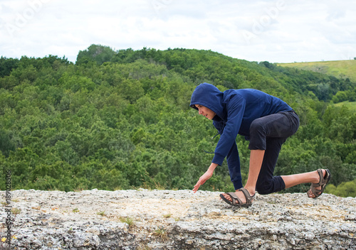 Boy, a teenager moves on bent legs along the edge of the cliff