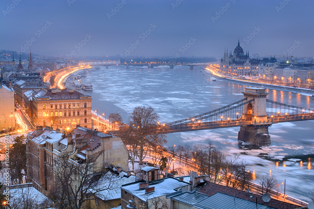 Old residential houses on Buda side, Danube river and Parliament outline. Winter night, Budapest